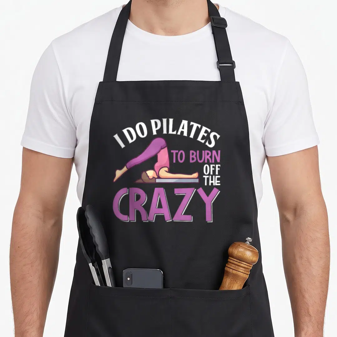 Trainer pilates apron - Cartoon woman in purple leggings lying on a mat under text reading I DO PILATES TO BURN OFF — shown on a black cotton canvas apron against a white background