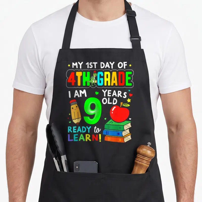 1st day fourth apron - Cartoon 9 with dinosaur pencil apple books and 1st day of 4th grade text — shown on a black cotton canvas apron against a white background