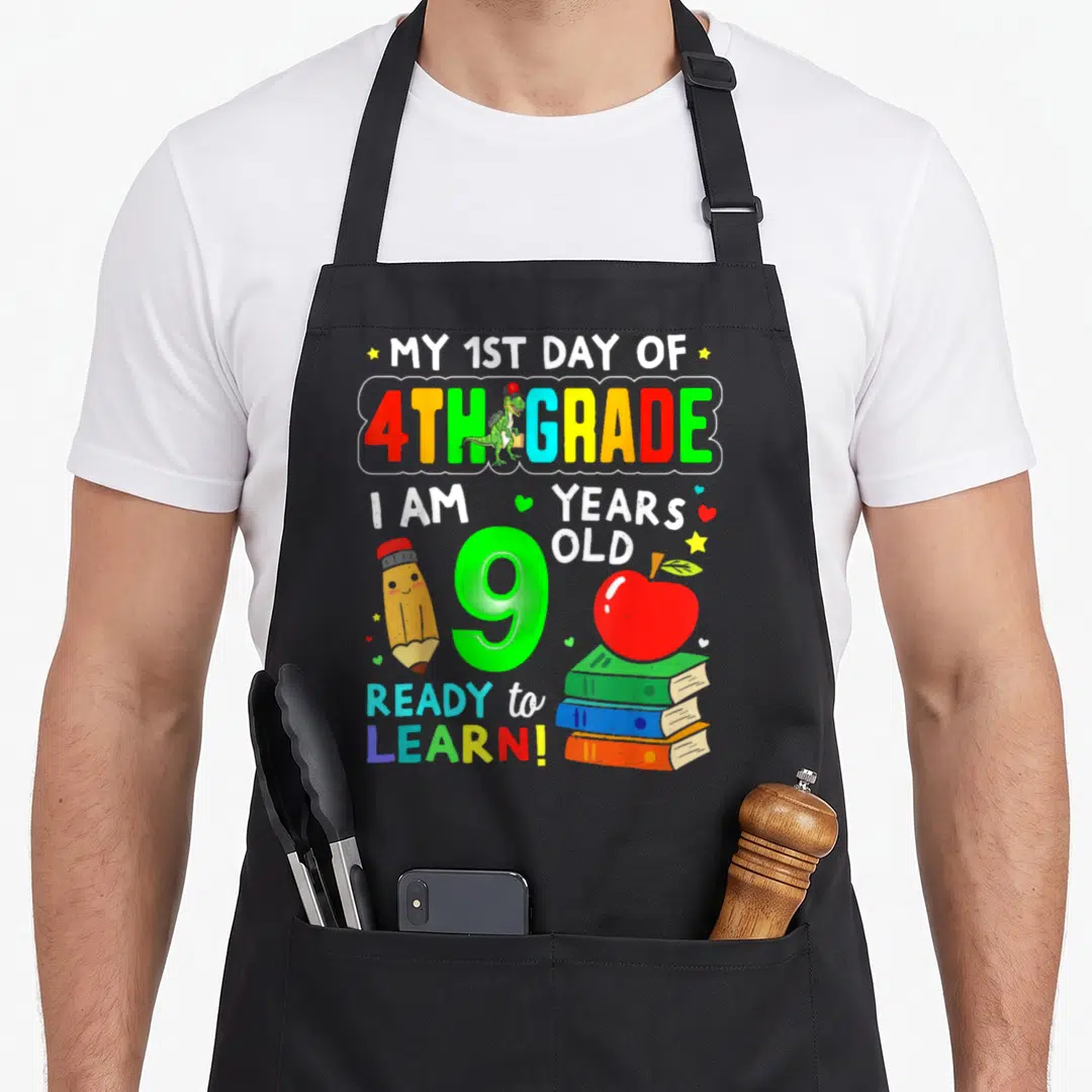 1st day fourth apron - Cartoon 9 with dinosaur pencil apple books and 1st day of 4th grade text — shown on a black cotton canvas apron against a white background