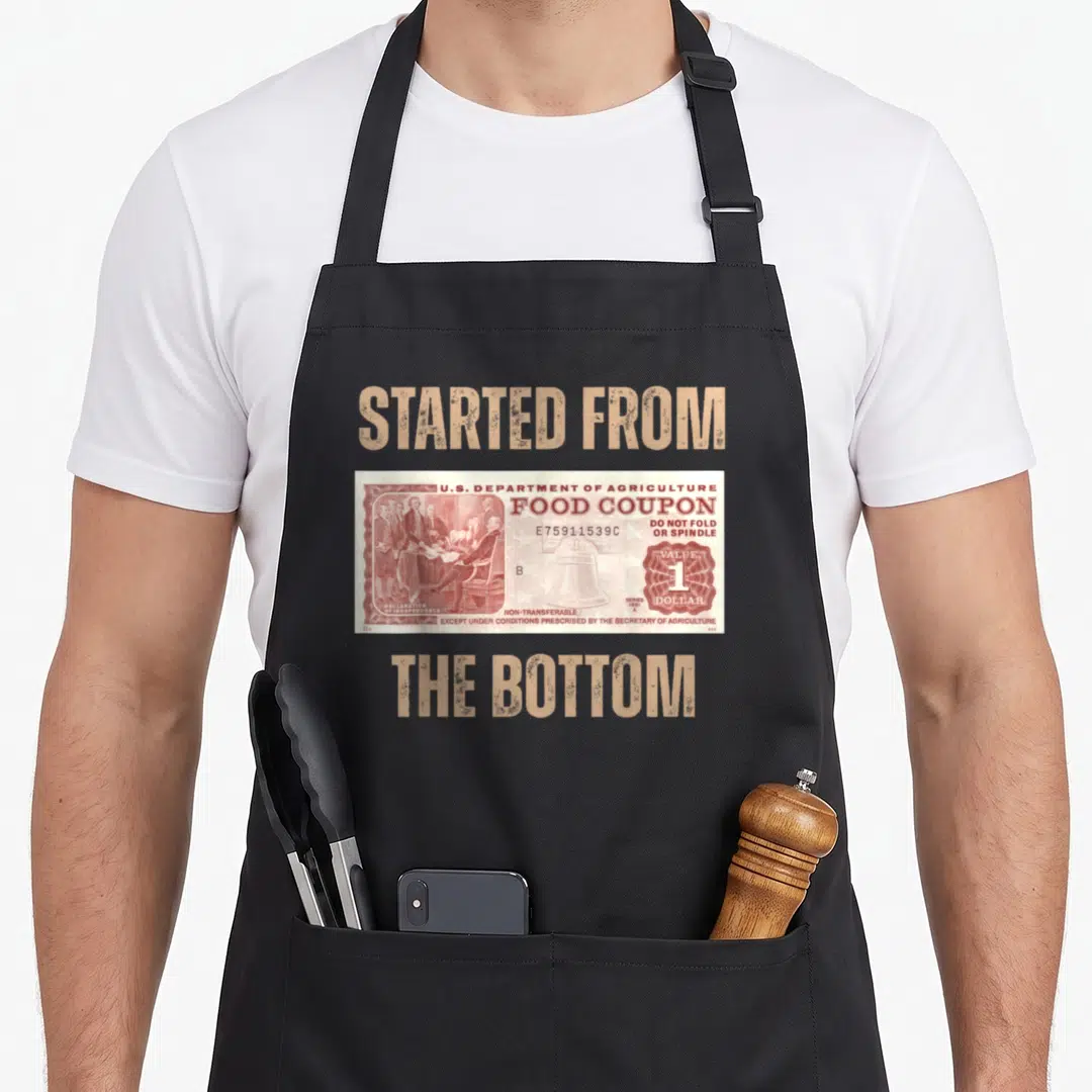 Stamp food aprons - Distressed tan text started from the bottom surrounding a red and white 1981 food coupon — shown on a black cotton canvas apron against a white background