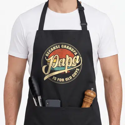 Sunset grandpa apron - Retro circular design with Papa text over red orange yellow teal striped sun — shown on a black cotton canvas apron against a white background