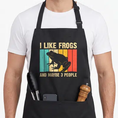 Amphibian frog aprons - Retro frog silhouette over teal beige yellow orange and red stripes with humorous text — shown on a black cotton canvas apron against a white background