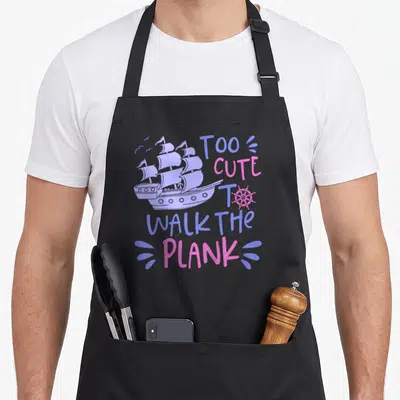 Walk pirate apron - Purple sailing ship and pink text reading Too Cute to Walk the Plank on black fabric — shown on a black cotton canvas apron against a white background