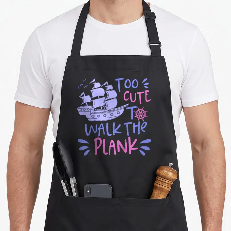 Walk pirate apron - Purple sailing ship and pink text reading Too Cute to Walk the Plank on black fabric — shown on a black cotton canvas apron against a white background