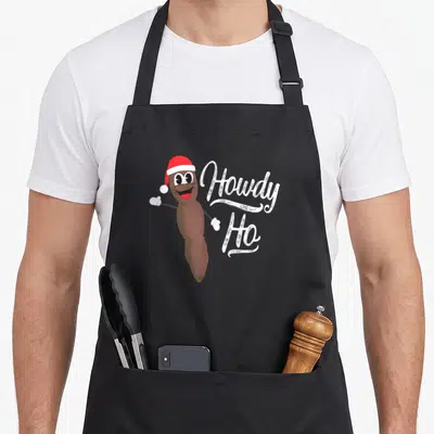 Hankey christmas apron - Brown poop emoji character wearing red Santa hat next to white Howdy Ho script text — shown on a black cotton canvas apron against a white background
