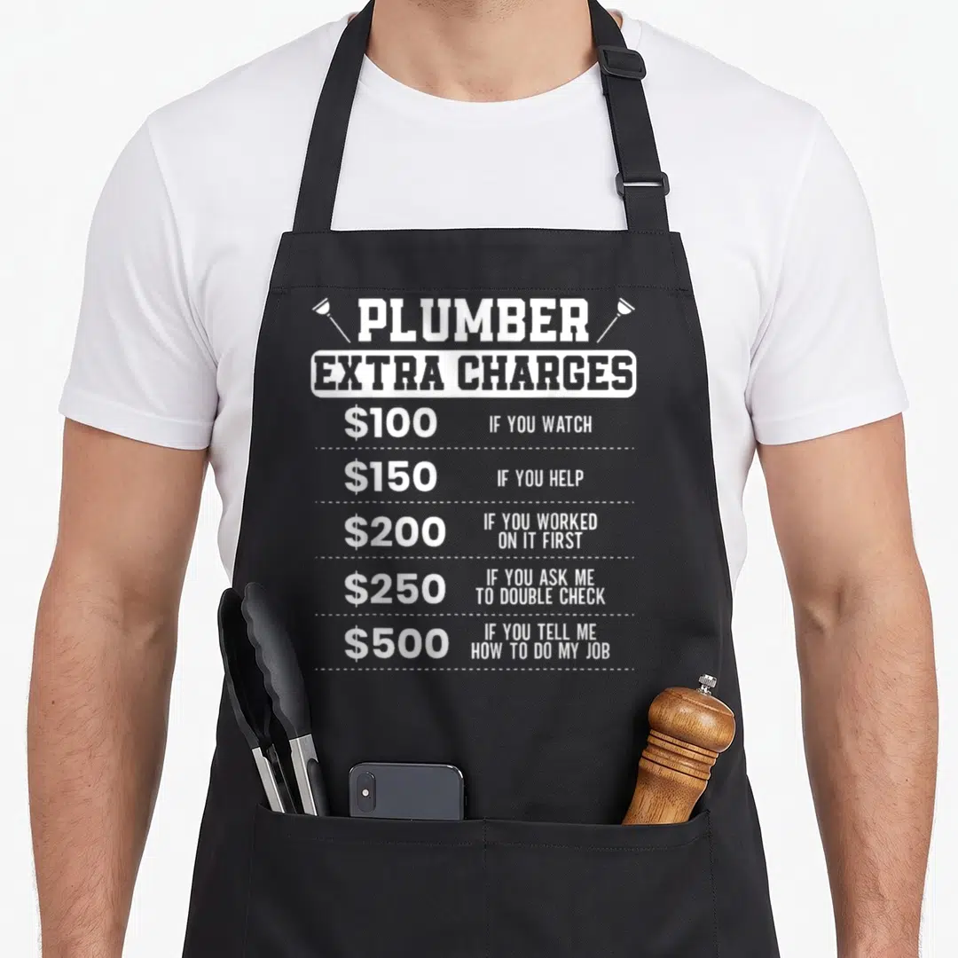 Plumber surgeon apron - White typography listing extra charges for watching helping and double checking plumbing work — shown on a black cotton canvas apron against a white background