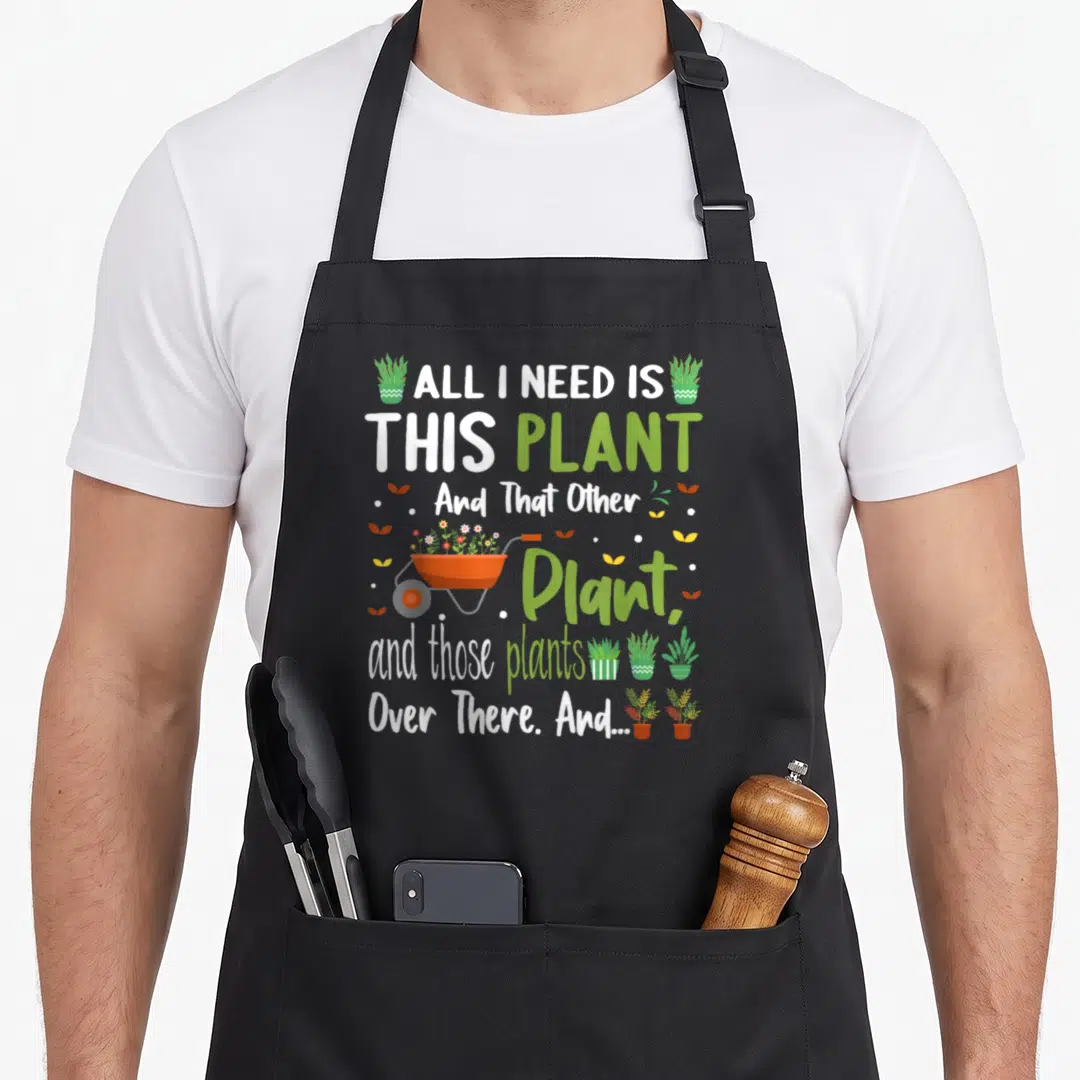 Vintage plant gardener apron - Cartoon text All I Need Is This Plant with potted plants and dots on black apron — shown on a black cotton canvas apron against a white background