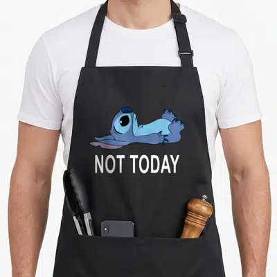 Today stitch apron - Blue cartoon character lying down above white NOT TODAY text — shown on a black cotton canvas apron against a white background