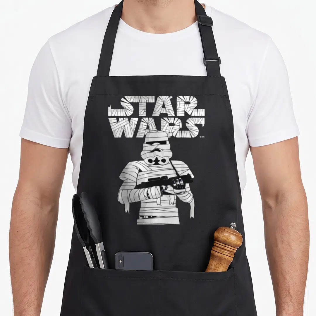 Halloween costume mummy and me aprons - Bandaged stormtrooper holding blaster under STAR WARS text filled with white — shown on a black cotton canvas apron against a white background