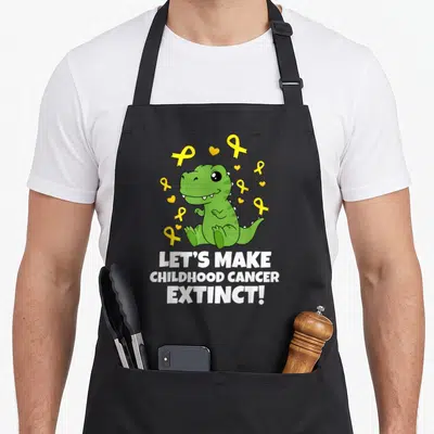 Extinct childhood cancer awareness apron - Green cartoon dinosaur surrounded by yellow ribbons and white text LET'S — shown on a black cotton canvas apron against a white background