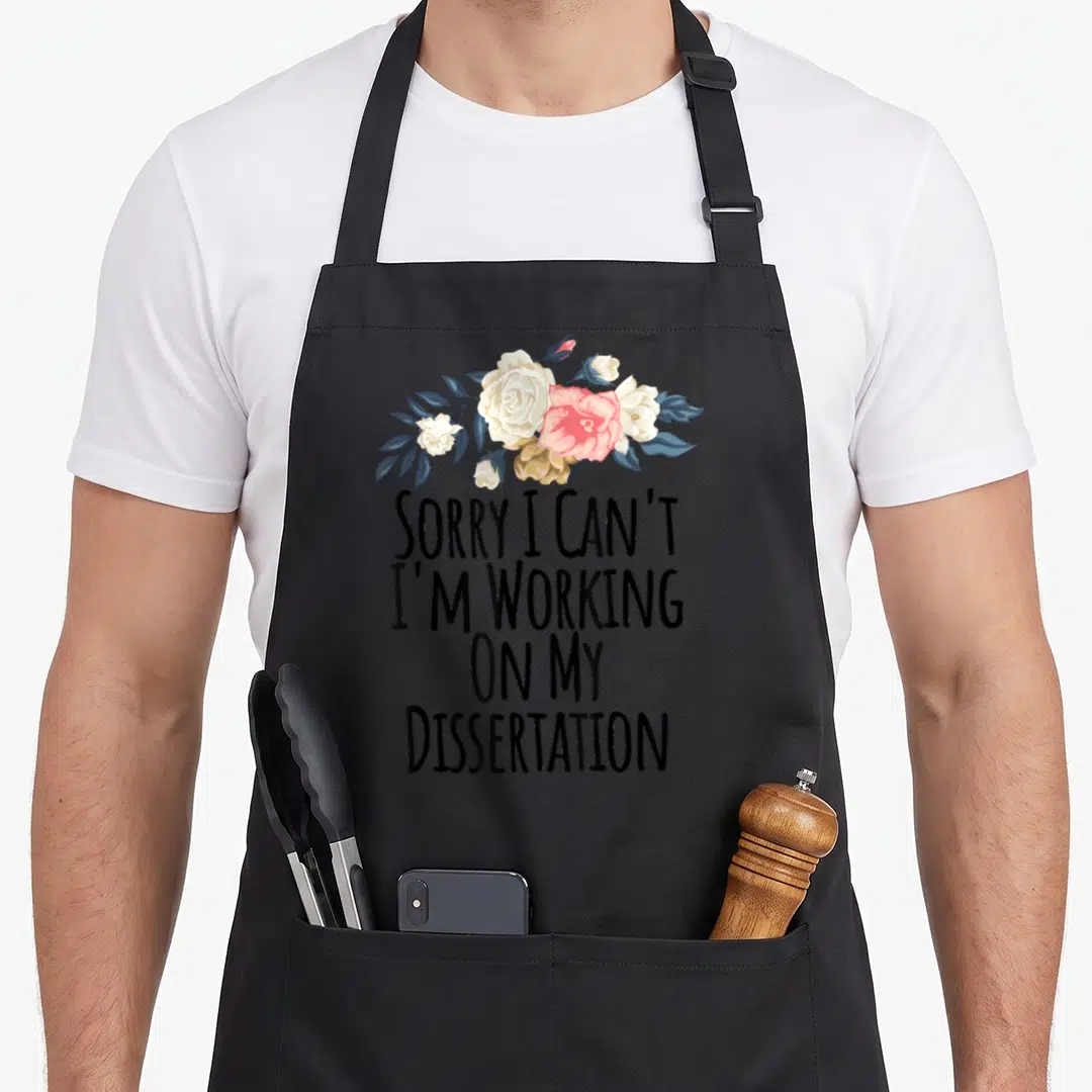 Sorry floral apron - SORRY I CAN'T I'M WORKING ON MY DISSERTATION text above pink white and blue-grey flower cluster — shown on a black cotton canvas apron against a white background