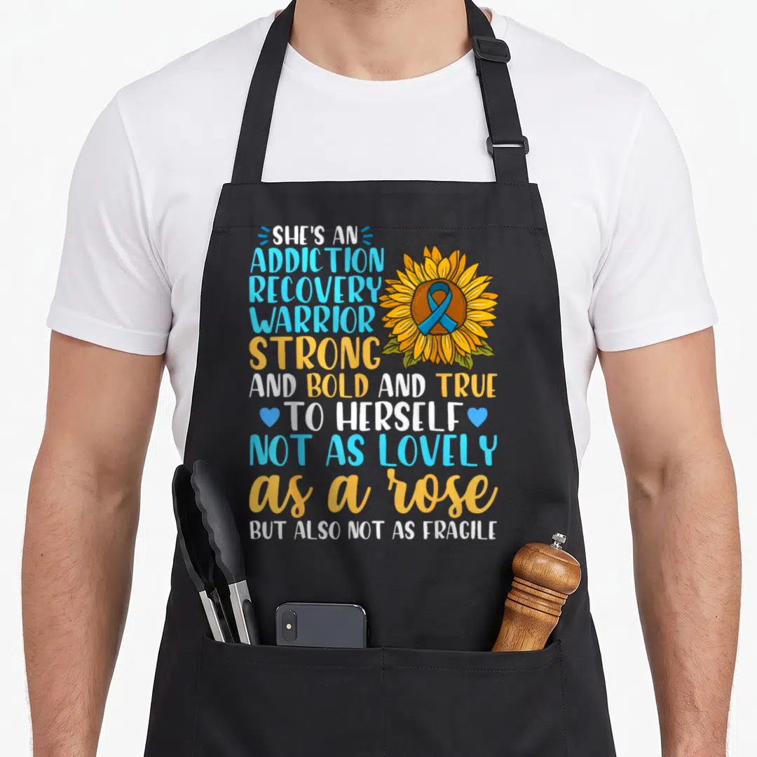 Drug alcohol recovery apron - Sunflower with blue ribbon and stacked recovery warrior text in yellow and blue — shown on a black cotton canvas apron against a white background