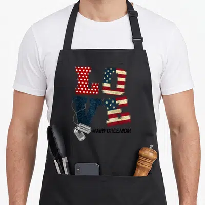 Proud usaf us aprons - Stacked LOVE typography with dog tags and AIRFORCEMOM hashtag in red white blue and silver — shown on a black cotton canvas apron against a white background