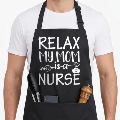 Relax white nurse apron - White stacked text reading RELAX MY MOM is a NURSE with a syringe and nurse hat graphic — shown on a black cotton canvas apron against a white background