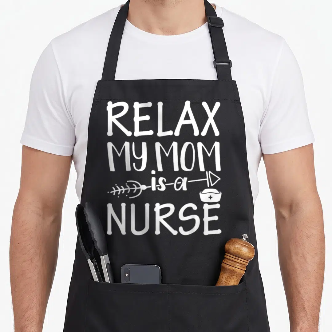 Relax white nurse apron - White stacked text reading RELAX MY MOM is a NURSE with a syringe and nurse hat graphic — shown on a black cotton canvas apron against a white background