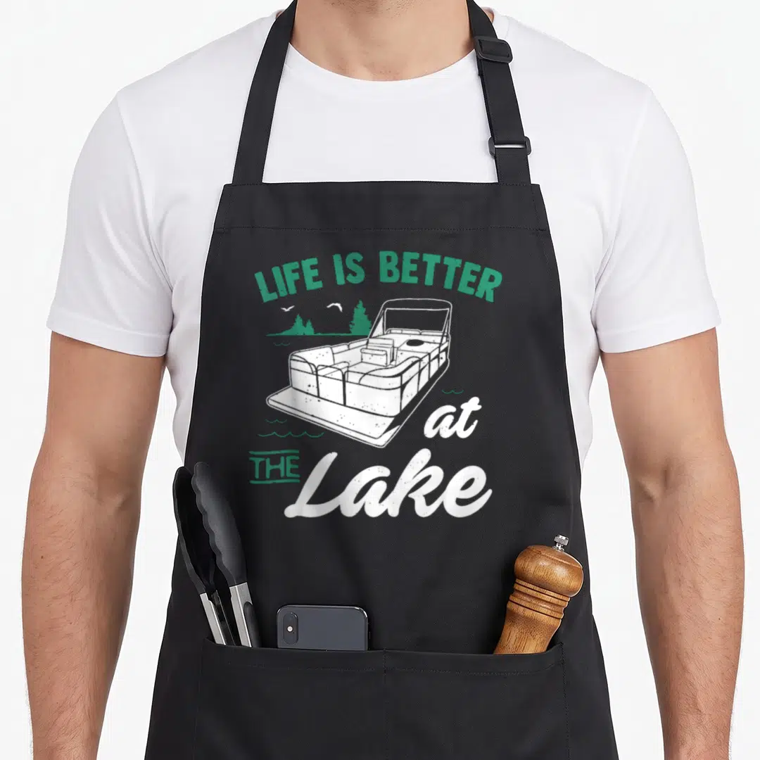 Better boat apron - Retro pontoon boat with LIFE IS BETTER at THE Lake text in green and white — shown on a black cotton canvas apron against a white background