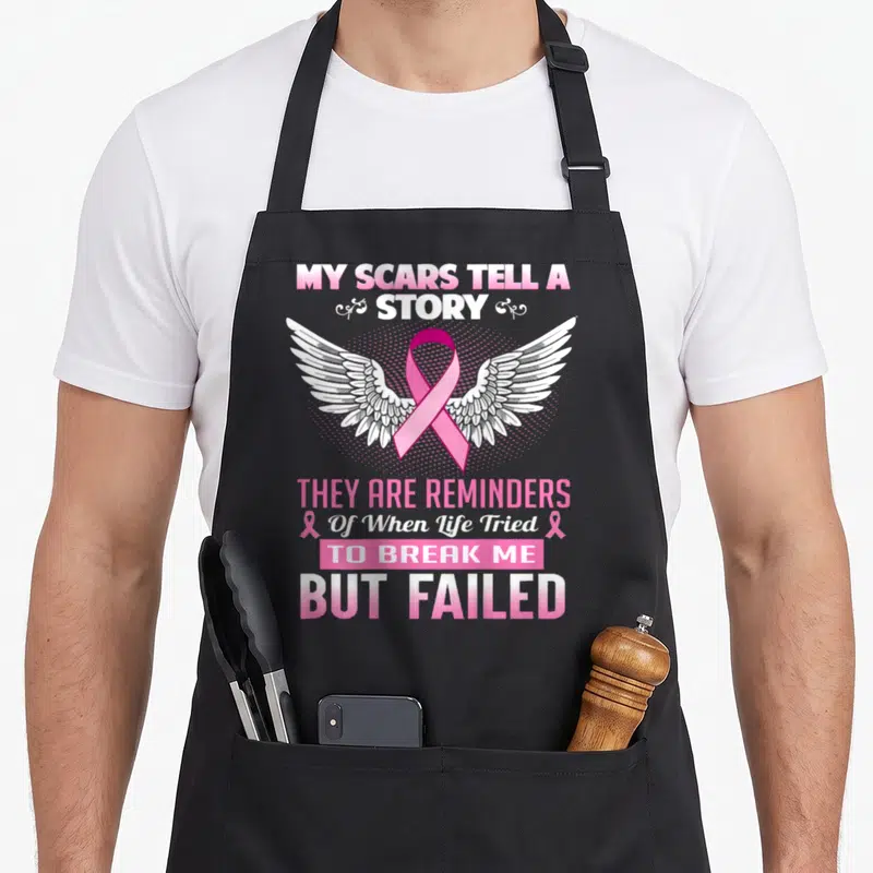 Scar breast cancer awareness aprons - Pink ribbon over white wings with My Scars Tell A Story text — shown on a black cotton canvas apron against a white background