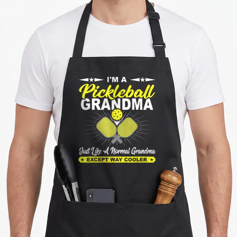 Grandma pickleball apron - Stacked text reading I'm a Pickleball Grandma above two crossed yellow paddles and a ball — shown on a black cotton canvas apron against a white background