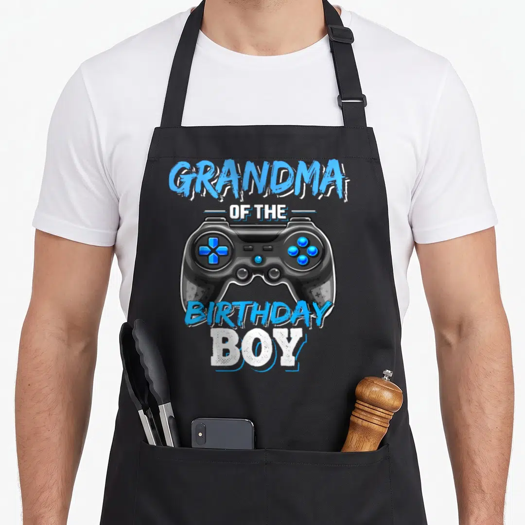 Video grandma in apron - Realistic black game controller with blue buttons and arched text reading GRANDMA — shown on a black cotton canvas apron against a white background