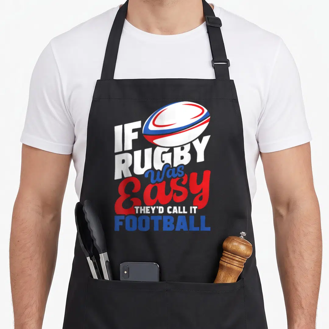 Call easy apron - Rugby ball above stacked text reading IF RUGBY Was Easy THEY'D CALL IT FOOTBALL in white red blue — shown on a black cotton canvas apron against a white background