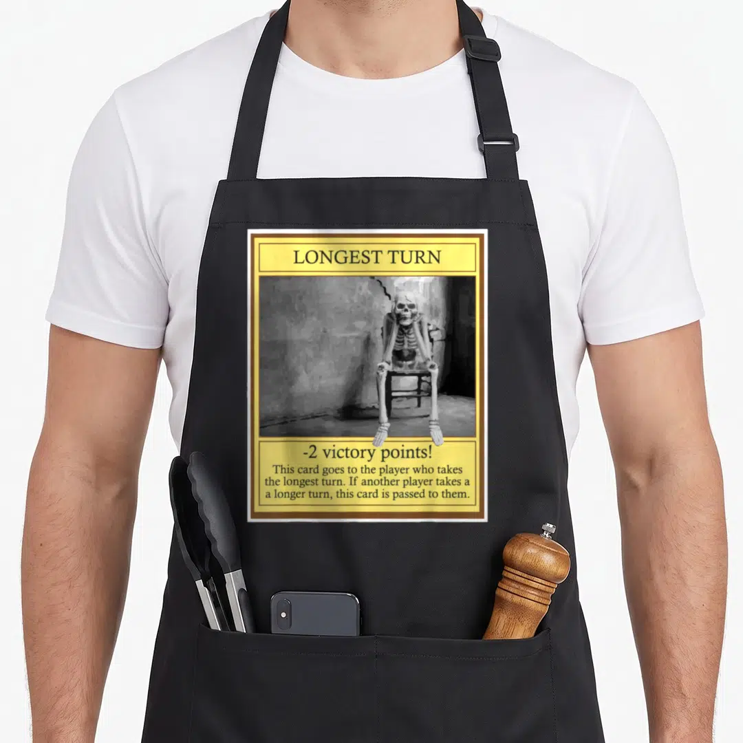 Longest i turn grills on apron - Yellow bordered game card with skeleton sitting in chair and longest turn penalty text — shown on a black cotton canvas apron against a white background