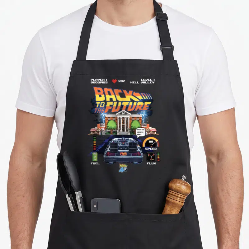 40th video game apron - Pixel art DeLorean and courthouse with Back to the Future HUD stats and text — shown on a black cotton canvas apron against a white background