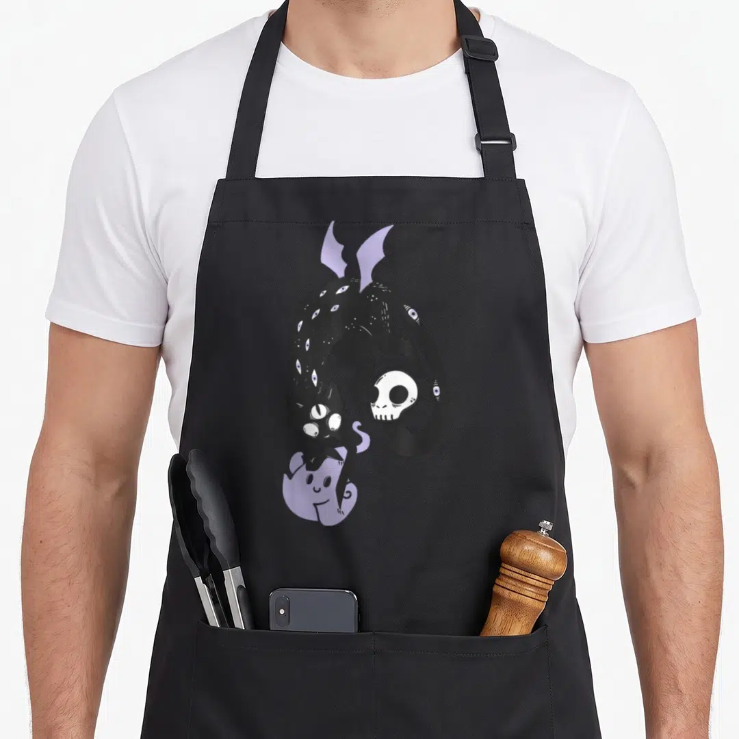 Cat goth apron - Black cat with multiple eyes curled around a skull and touching a purple ghost — shown on a black cotton canvas apron against a white background