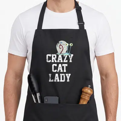 Gary crazy cat lady apron - Distressed snail above white stacked text CRAZY CAT LADY on black fabric — shown on a black cotton canvas apron against a white background