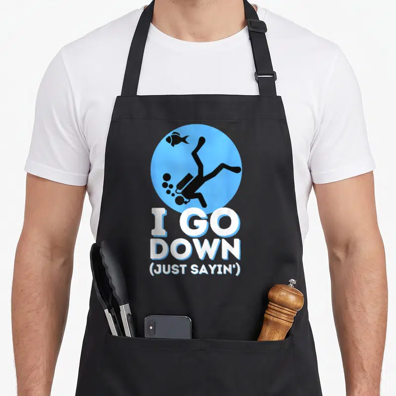 Sayin snorkeling apron - Cartoon diver in blue circle above I GO DOWN JUST SAYIN text — shown on a black cotton canvas apron against a white background