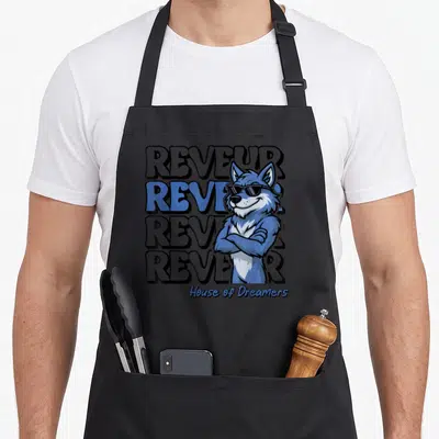 Dreamer student teacher apron - Stacked Reveur text with a blue cartoon wolf wearing sunglasses — shown on a black cotton canvas apron against a white background