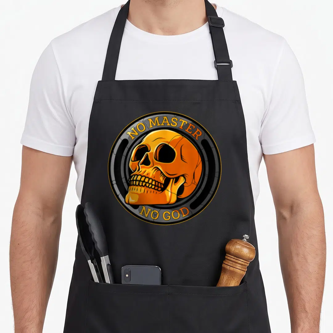 Atheist master apron - Orange cartoon skull inside grey circle with arched text no master no god — shown on a black cotton canvas apron against a white background