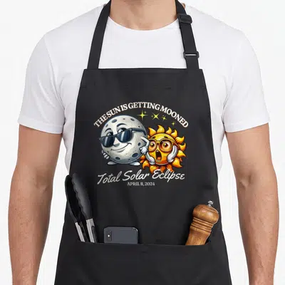 Sun april apron - Cartoon moon mooning sun with Total Solar Eclipse April 8 2024 text — shown on a black cotton canvas apron against a white background