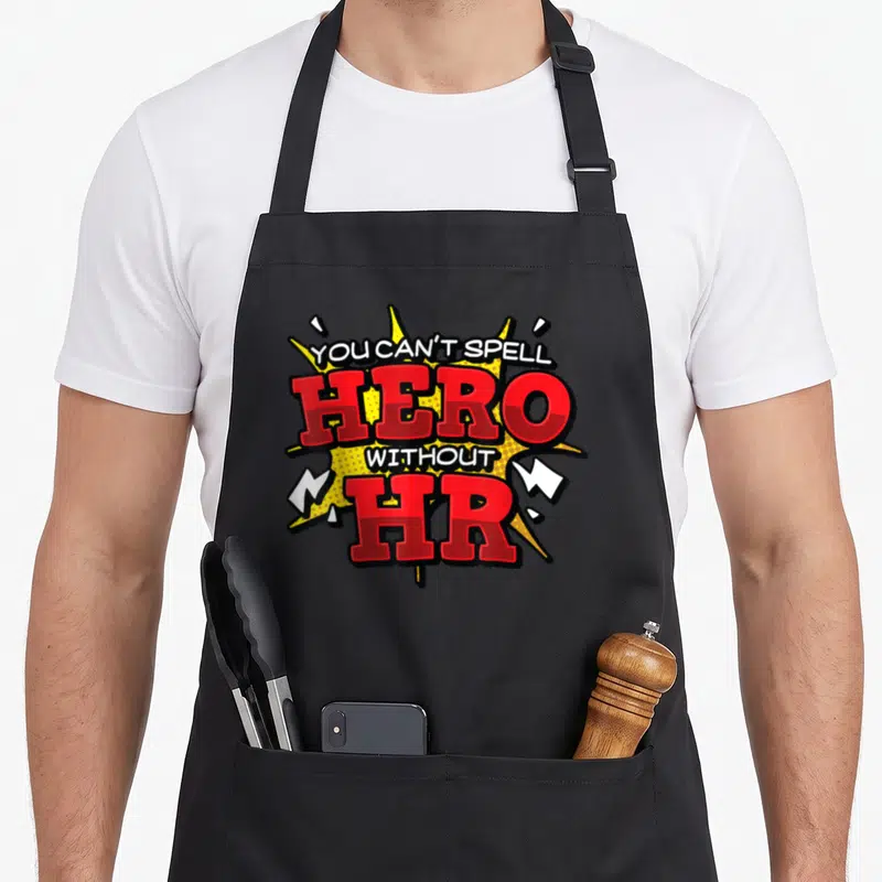 Spell hr apron - Comic burst graphic with stacked text reading YOU CAN'T SPELL HERO WITHOUT HR in red and white — shown on a black cotton canvas apron against a white background
