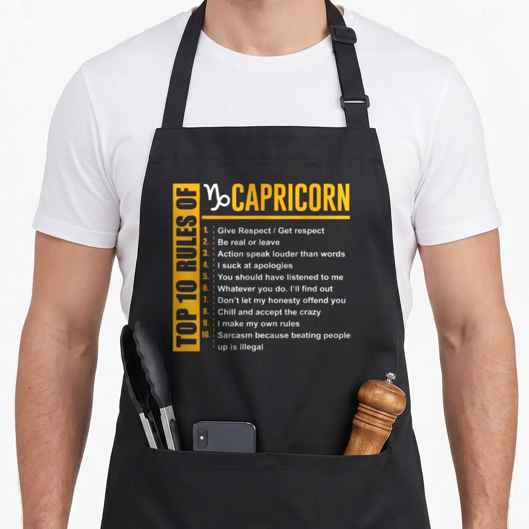 Rule capricorn birthday apron - Yellow and white typography listing ten Capricorn rules including sarcasm and respect — shown on a black cotton canvas apron against a white background