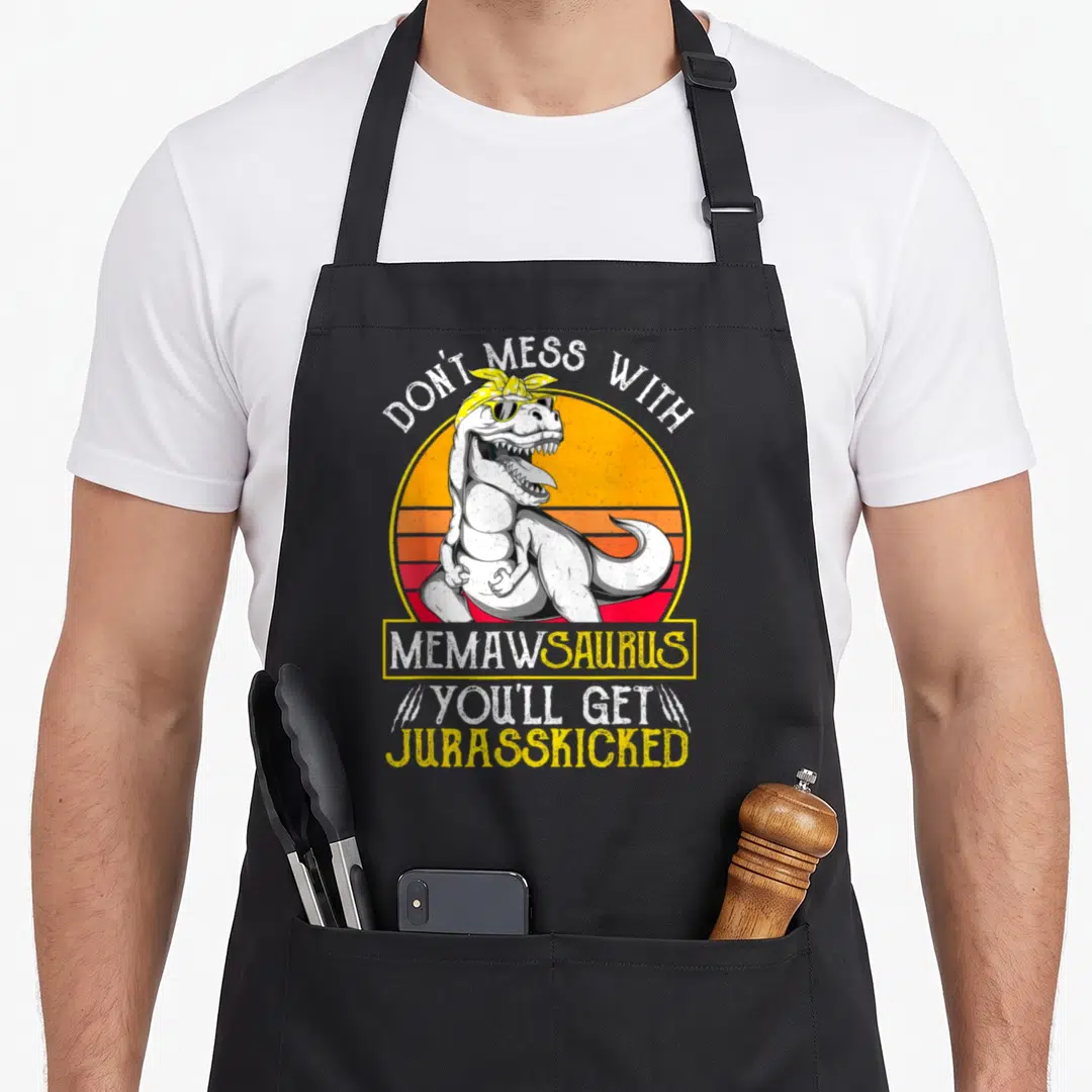 Jurasskicked grandma apron - T-Rex with sunglasses in front of striped sun with text Don't Mess With Memawsaurus — shown on a black cotton canvas apron against a white background