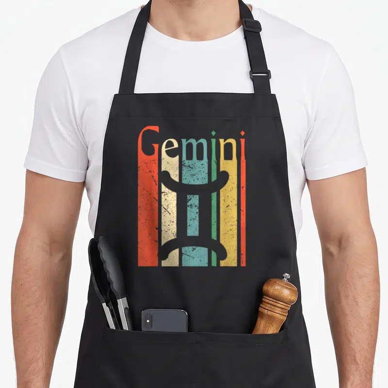 Funny gemini zodiac aprons - Retro Gemini symbol over five vertical stripes in red, cream, teal, yellow, and grey — shown on a black cotton canvas apron against a white background