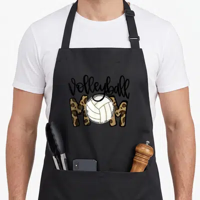 Volleyball leopard print cooking apron - Volleyball MOM text with white ball over tan leopard print letters — shown on a black cotton canvas apron against a white background