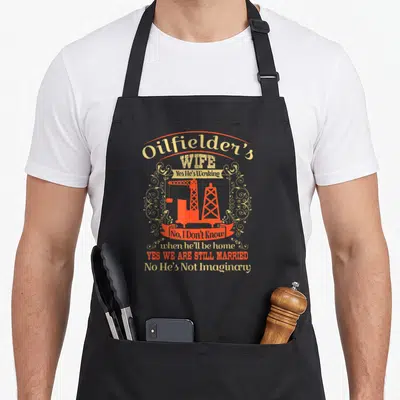 Hes wife apron - Retro orange oil rig with sarcastic text about a working husband and marriage status — shown on a black cotton canvas apron against a white background
