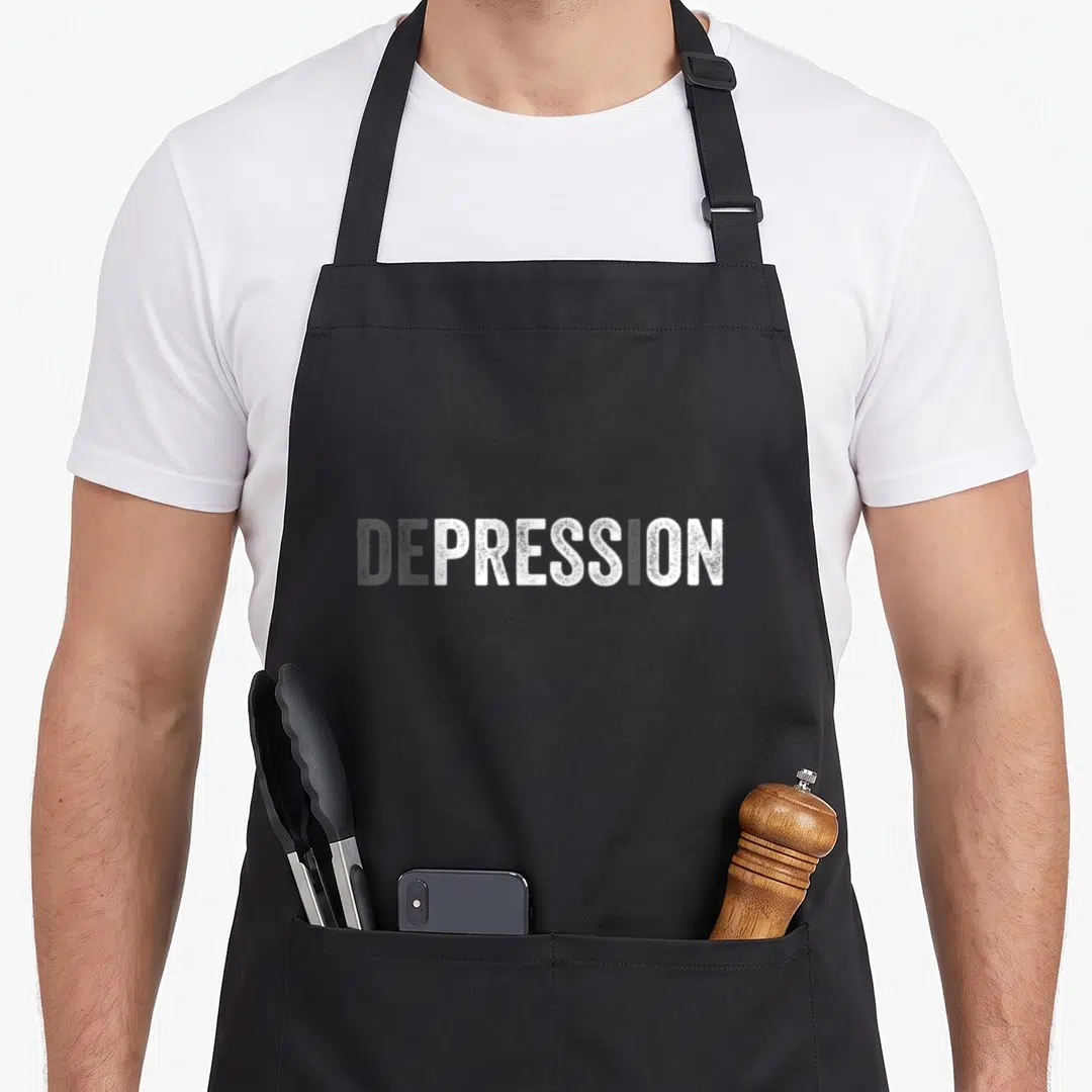 National education apron - White distressed typography reading DEPRESSION on dark grey background — shown on a black cotton canvas apron against a white background