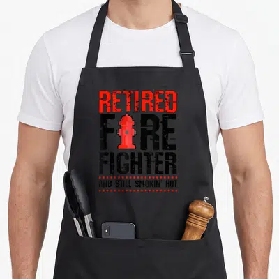 Fireman retirement firefighter cooking apron - Red hydrant replacing I in black FIRE text with red dots and distressed — shown on a black cotton canvas apron against a white background