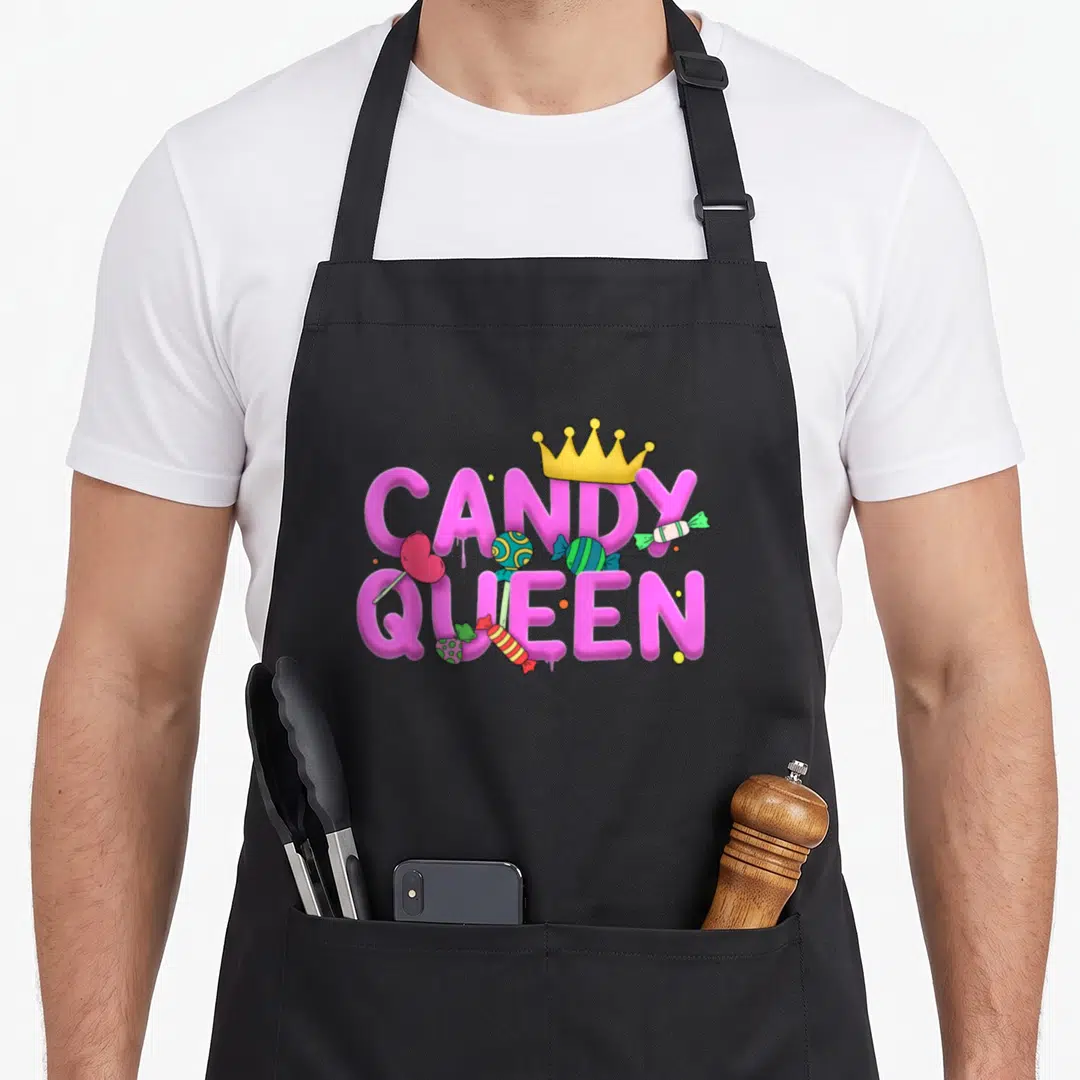 Lollipop candy aprons - Pink CANDY QUEEN text with yellow crown and scattered cartoon sweets in blue and green — shown on a black cotton canvas apron against a white background