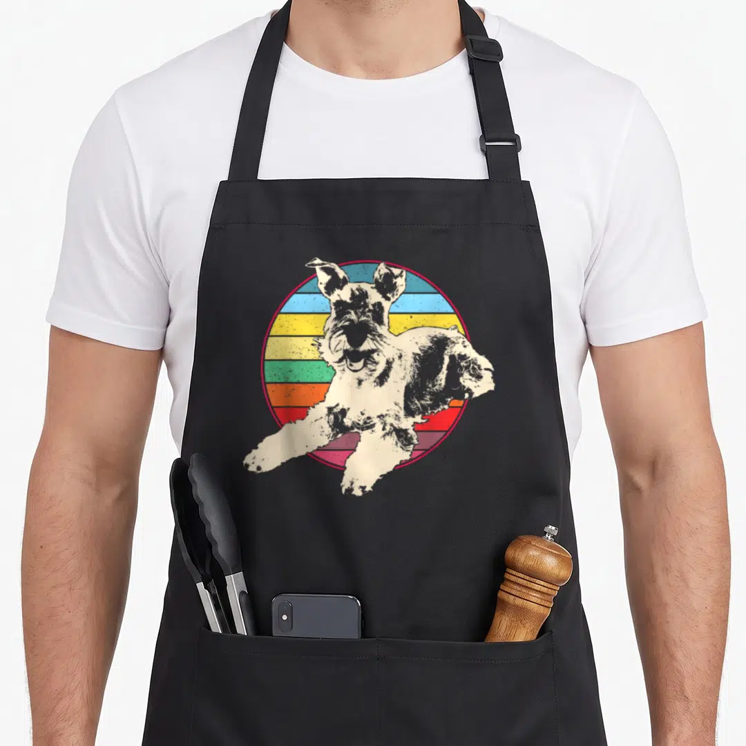 Standard dog miniature schnauzer apron - Beige dog jumping in front of a multi-colored striped circle with a red border — shown on a black cotton canvas apron against a white background