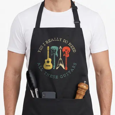 Funny guitarist guitar apron - Four colorful guitars in beige teal yellow and red with arching retro text — shown on a black cotton canvas apron against a white background