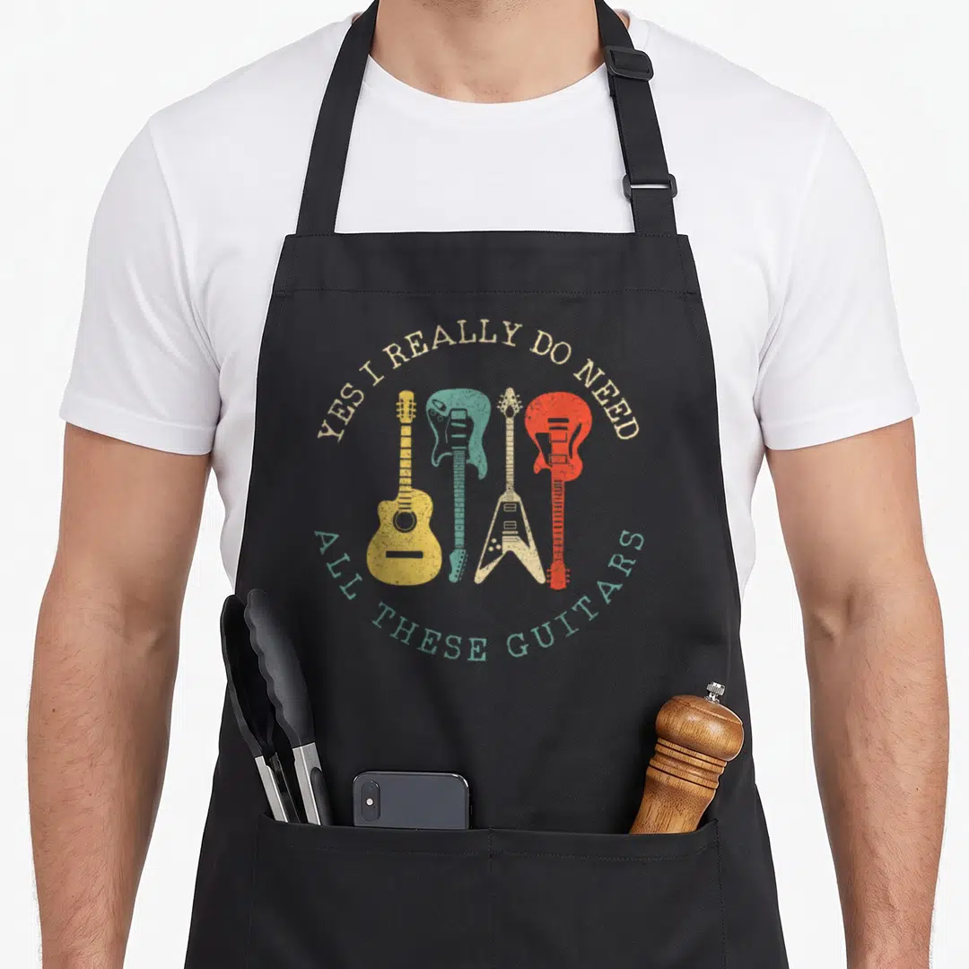 Funny guitarist guitar apron - Four colorful guitars in beige teal yellow and red with arching retro text — shown on a black cotton canvas apron against a white background