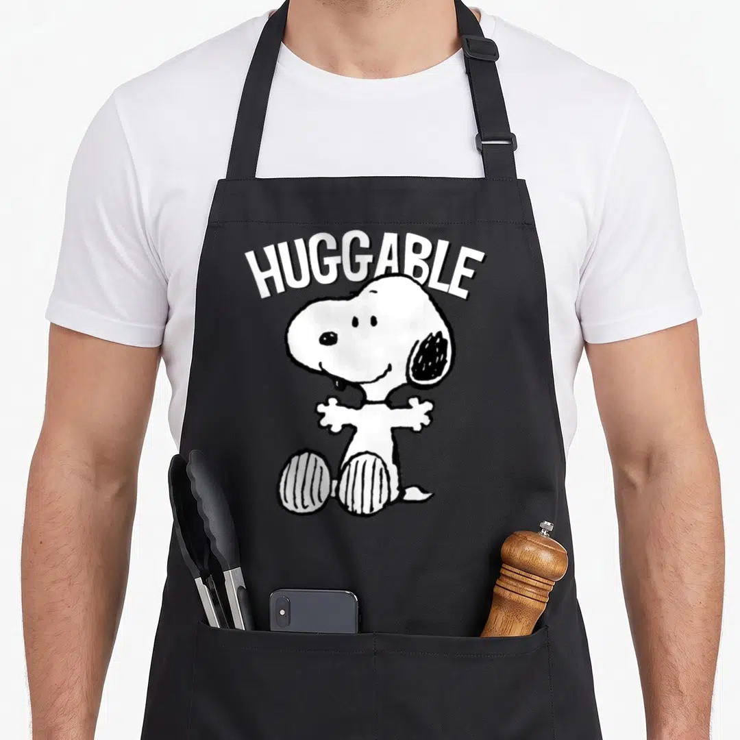 Huggable mother's apron - Arched HUGGABLE text above seated cartoon dog with open arms in white and black — shown on a black cotton canvas apron against a white background
