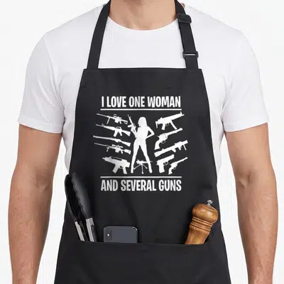 Gun husband apron - White silhouette of woman holding rifle surrounded by gun shapes and ironic text — shown on a black cotton canvas apron against a white background