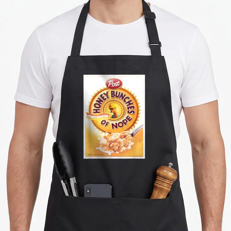 Honey breakfast apron - Cereal box parody with Post HONEY BUNCHES OF NOPE text and man in hard hat — shown on a black cotton canvas apron against a white background