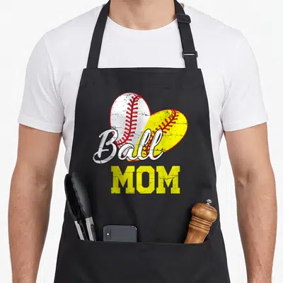 Ball mother's day aprons - Distressed Ball MOM text over split heart baseball and softball in yellow white red — shown on a black cotton canvas apron against a white background