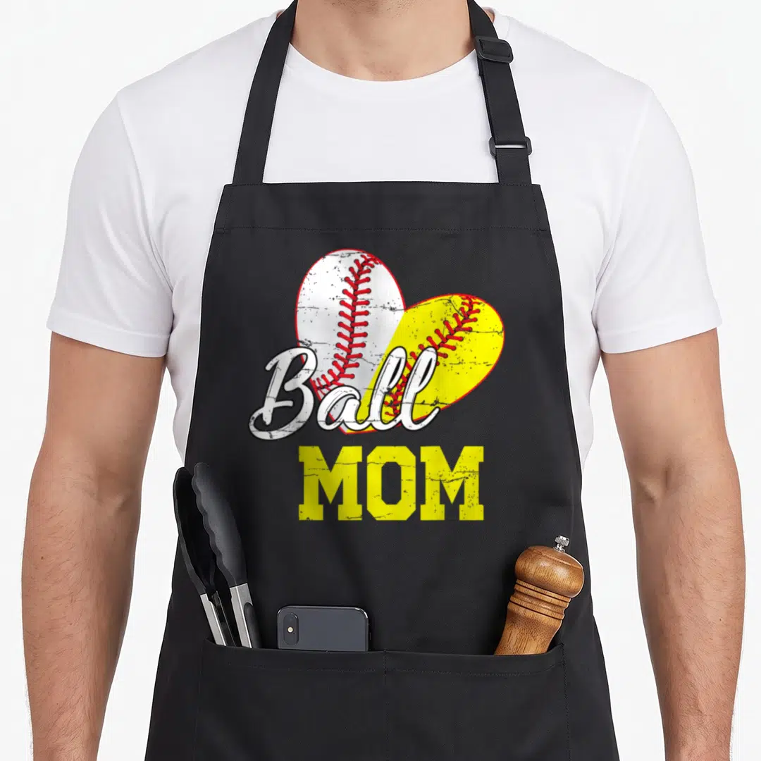 Ball mother's day aprons - Distressed Ball MOM text over split heart baseball and softball in yellow white red — shown on a black cotton canvas apron against a white background