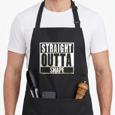 Straight joke apron - Stacked white and olive green distressed text reading STRAIGHT OUTTA SHAPE inside a rectangle — shown on a black cotton canvas apron against a white background